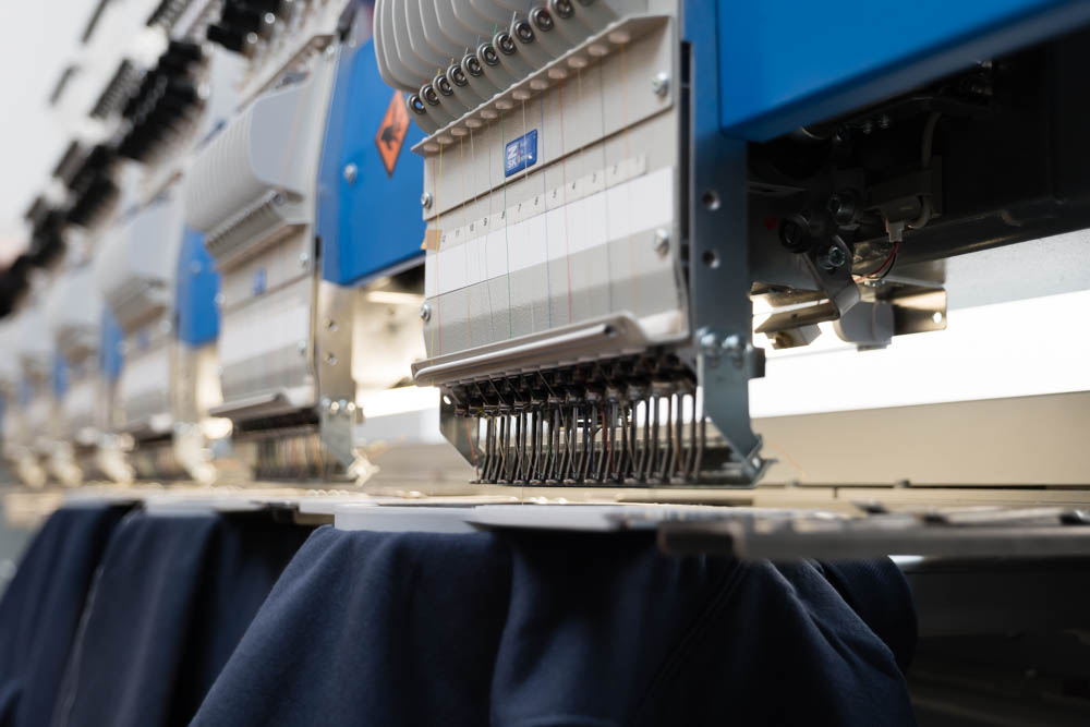 moderne Stickmaschinen bearbeiten mit mehreren hochwertigen Stickereien auf edlen blauen Poloshirts
